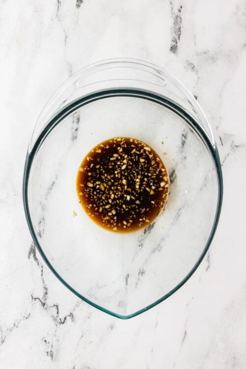 Soy sauce marinade with garlic and ginger in a glass bowl on marble surface, Asian cooking ingredient.