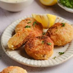 Golden crispy crab cakes with lemon wedges on a white plate.