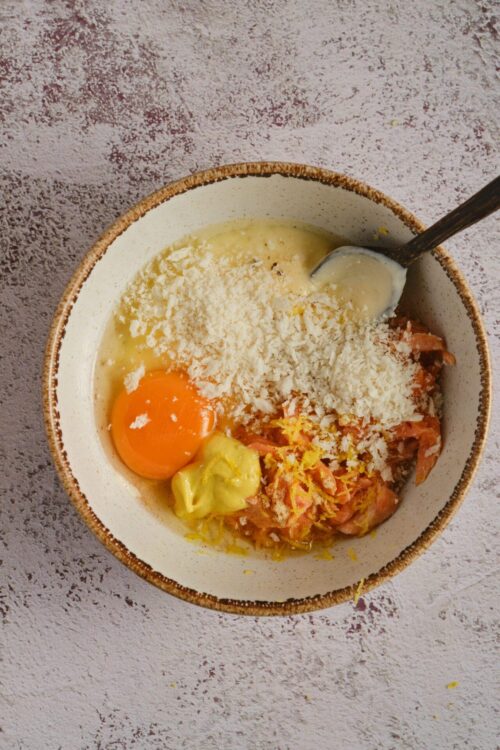 Cream cheese, eggs, smoked salmon, and grated cheese in a mixing bowl for homemade breakfast.
