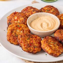 Crispy crab cakes with creamy dipping sauce on a white plate.