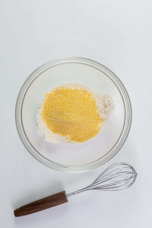 Colorful mixture of baking ingredients in a glass bowl with a whisk on a white background.