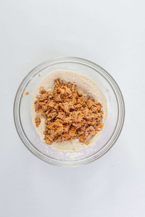 Crumbled cooked salmon mixed with flour in a glass bowl for baking or cooking recipes.