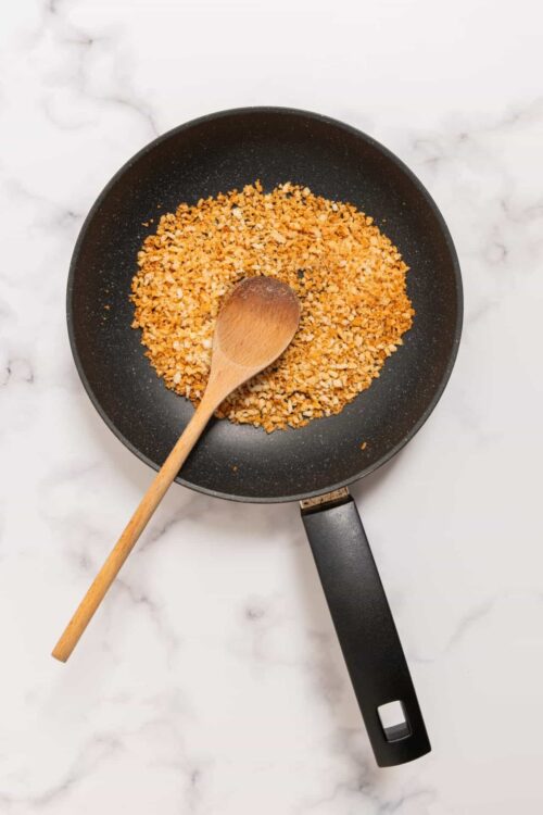 Golden toasted breadcrumbs in a black skillet on white marble surface.