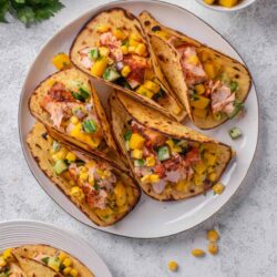Tender grilled fish tacos with mango salsa and fresh herbs on a white plate.