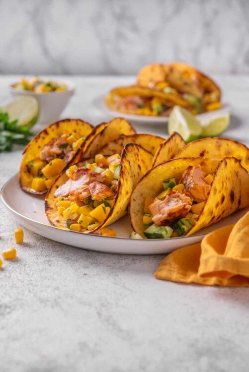Golden crispy taco shells filled with grilled chicken, corn, and fresh vegetables on a white plate.