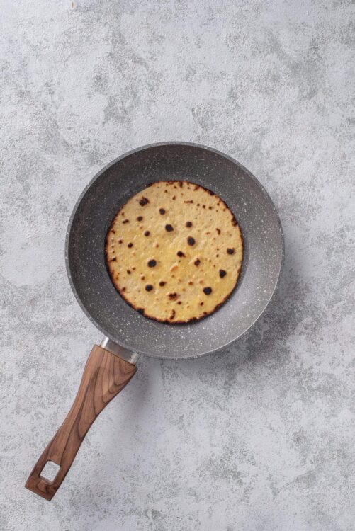 Golden toasted flatbread cooking in a non-stick pan on a gray textured surface.