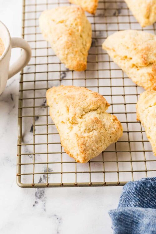 Fluffy homemade scones cooling on a wire rack with a cup of coffee nearby.
