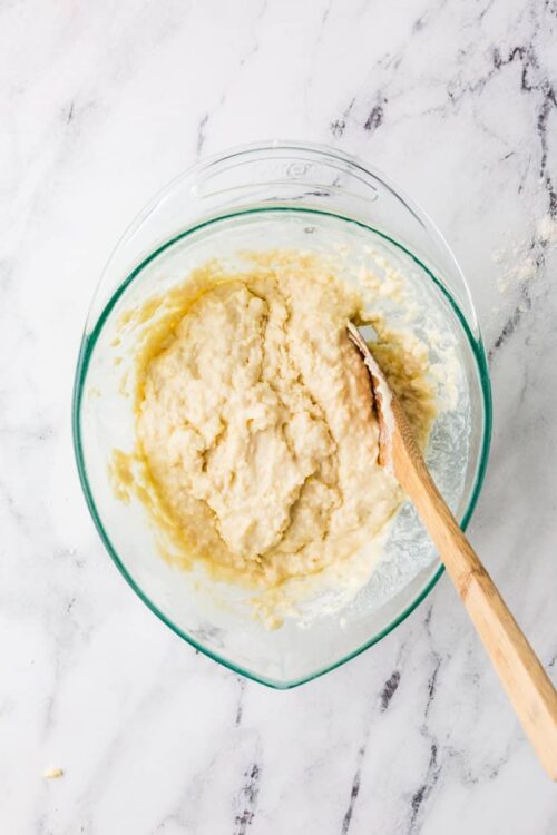 Creamy mashed potatoes in a glass mixing bowl with a wooden spoon.