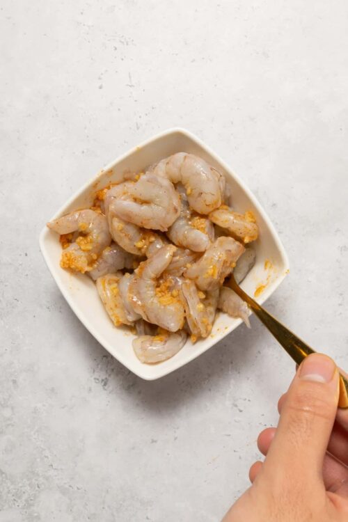Raw shrimp marinating with garlic in a white bowl.