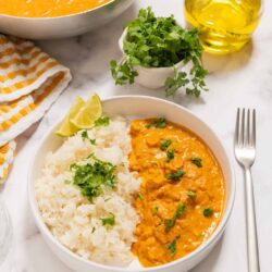 Savory chicken curry with rice in a white bowl, garnished with cilantro and lemon wedges.