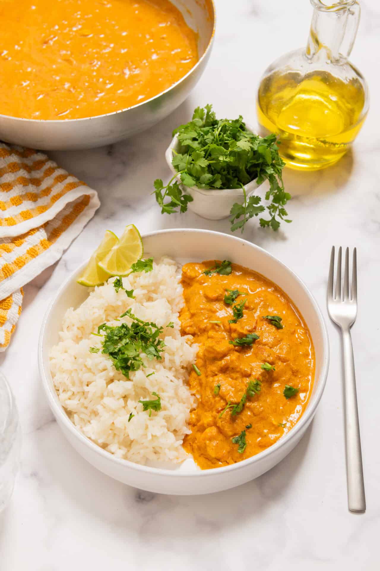 Savory chicken curry with rice in a white bowl, garnished with cilantro and lemon wedges.