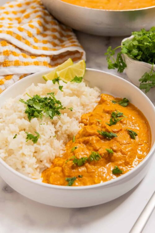 Creamy chicken curry with rice and cilantro in a white bowl.