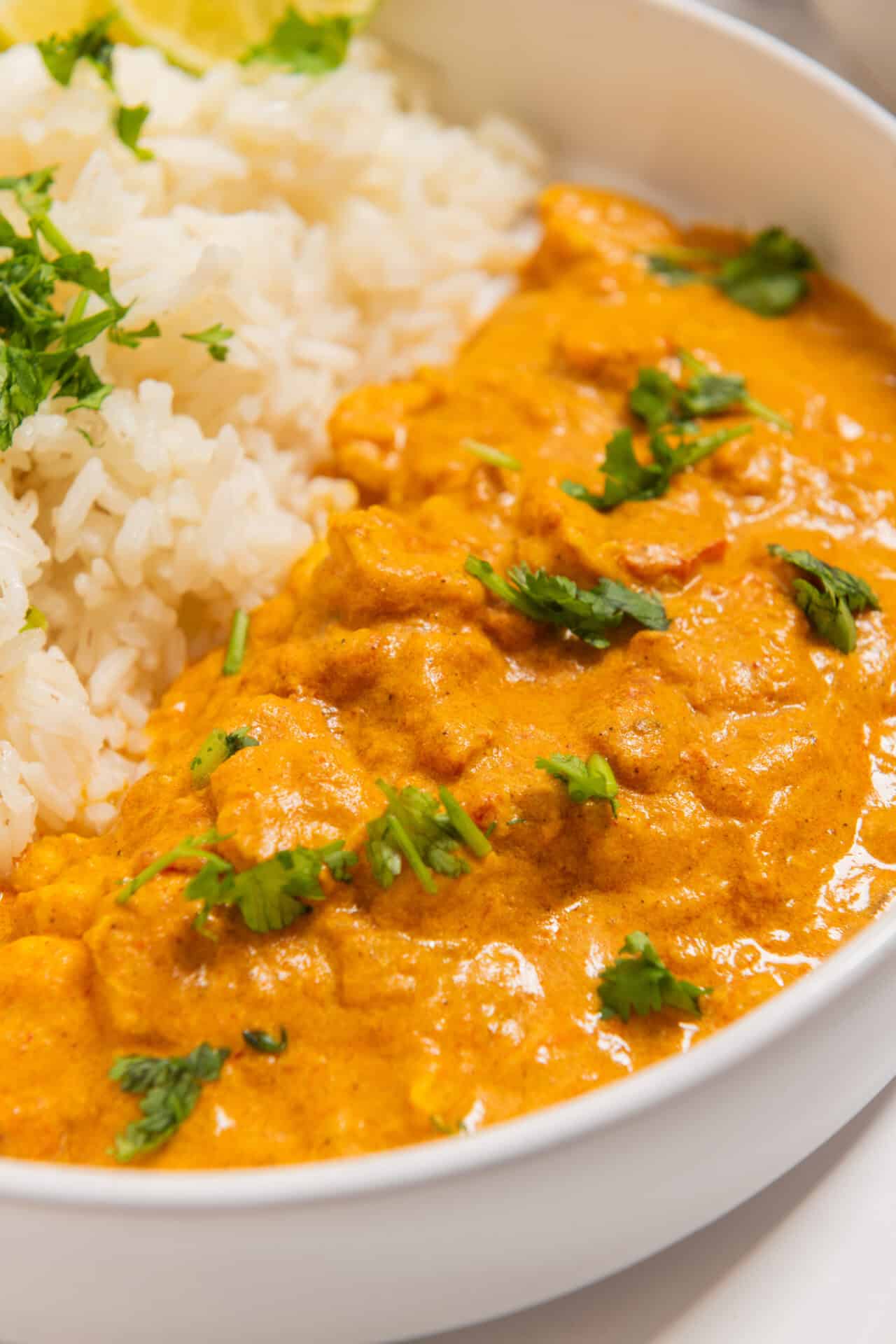 Creamy chicken curry with rice and fresh cilantro in a white bowl.