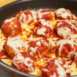 Savory homemade meatballs in marinara sauce with melted mozzarella cheese on top.