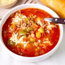 Savory homemade chili with ground beef, vegetables, and melted cheese in a white bowl, served with cornbread and shredded cheese on the side.