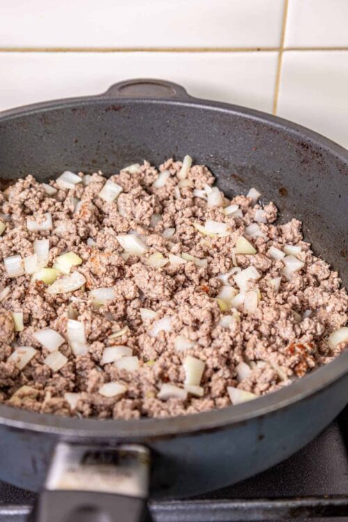 Ground beef cooking with diced onions in a black skillet.