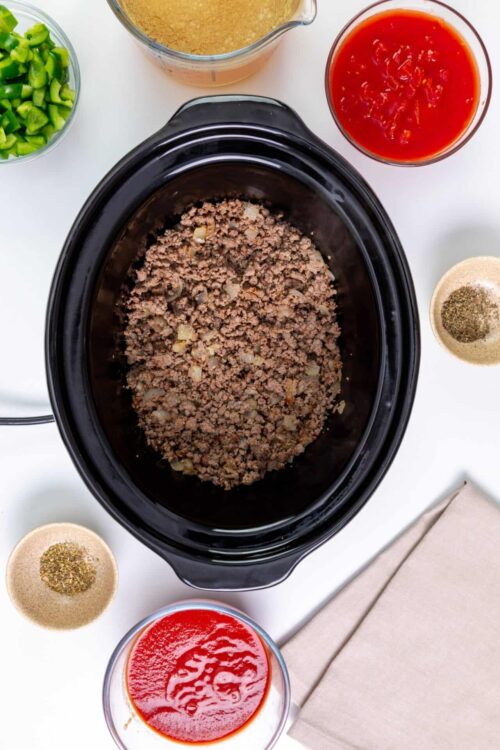 Cooked ground beef in slow cooker with chopped onions and seasonings.