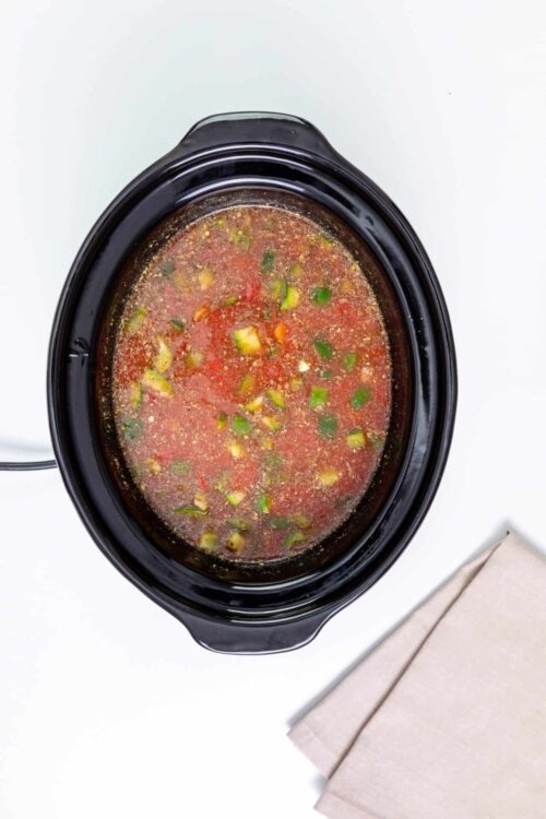 Savory slow cooker salsa chicken in black crockpot with fresh vegetables and herbs.