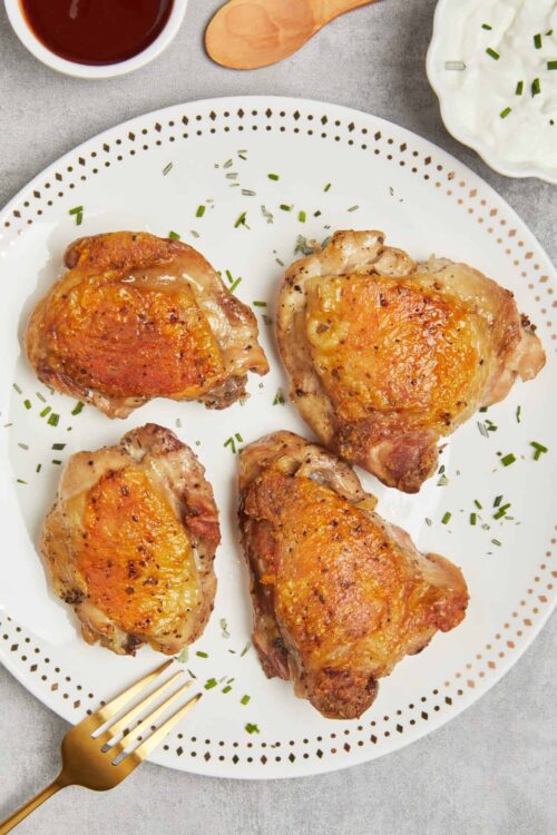 Juicy baked chicken thighs with golden crispy skin, seasoned to perfection and served on a white decorative plate.
