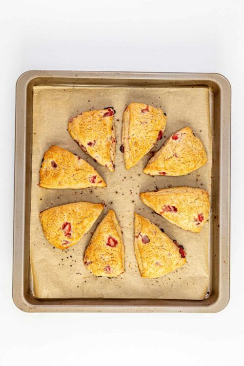 Buttery baked strawberry scones on baking sheet with parchment paper.