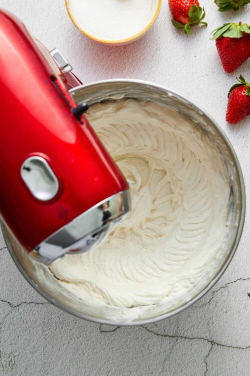 Cream cheese frosting being mixed with a red stand mixer, with fresh strawberries around.