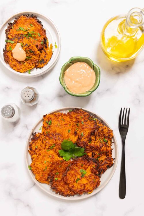 Crispy vegetable fritters with dipping sauces on white plate and marble countertop.
