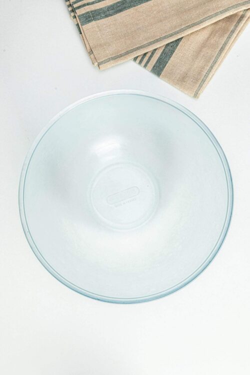 Clear glass mixing bowl with beige and green striped cloth napkin on white surface, ideal for baking and kitchen prep.