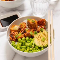 Baked tofu and vegetable rice bowl with green peas and avocado.