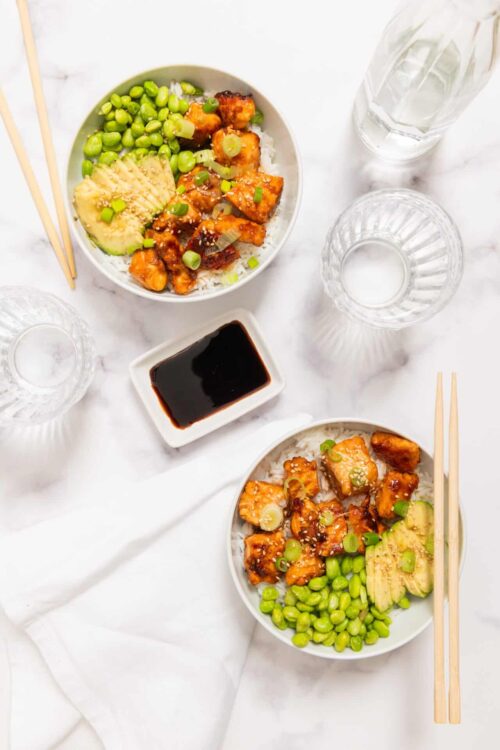 Crispy tofu Buddha bowl with rice, avocado, green peas, and sesame seeds, Asian-inspired vegetarian meal.