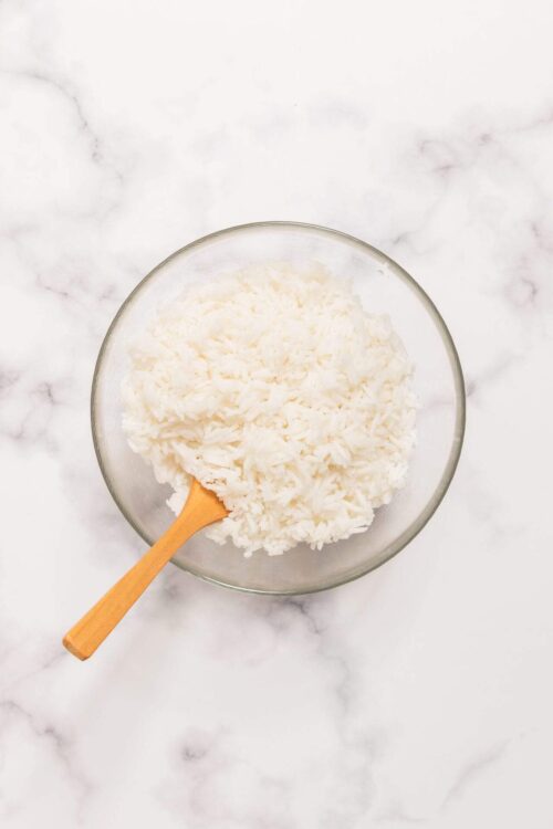 Fluffy cooked white rice in glass bowl on marble surface.