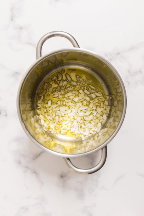 Minced garlic and chopped onions sautéing in olive oil in a stainless steel pot.