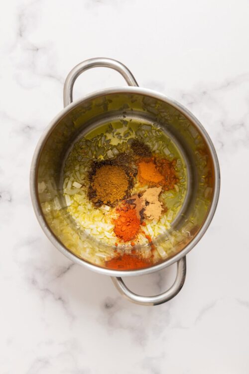 Golden sautéed onions and garlic with turmeric, paprika, and cayenne pepper in a stainless steel pot for flavorful cooking.