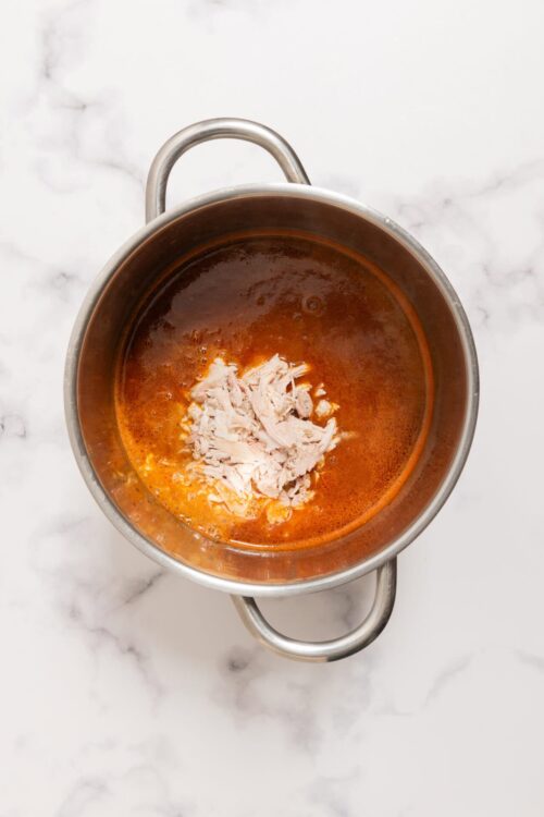 Shredded cooked chicken in spicy tomato broth in a stainless steel pot.