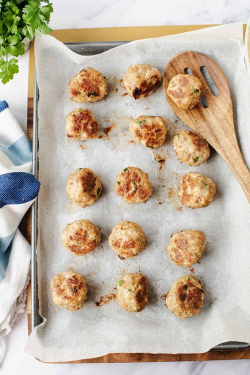 Cream cheese stuffed chicken meatballs on baking tray with parchment paper and wooden spatula.