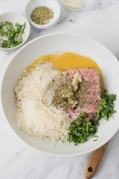 Freshly prepared meat mixture with herbs and cheese in a white bowl, ready for baking or cooking.