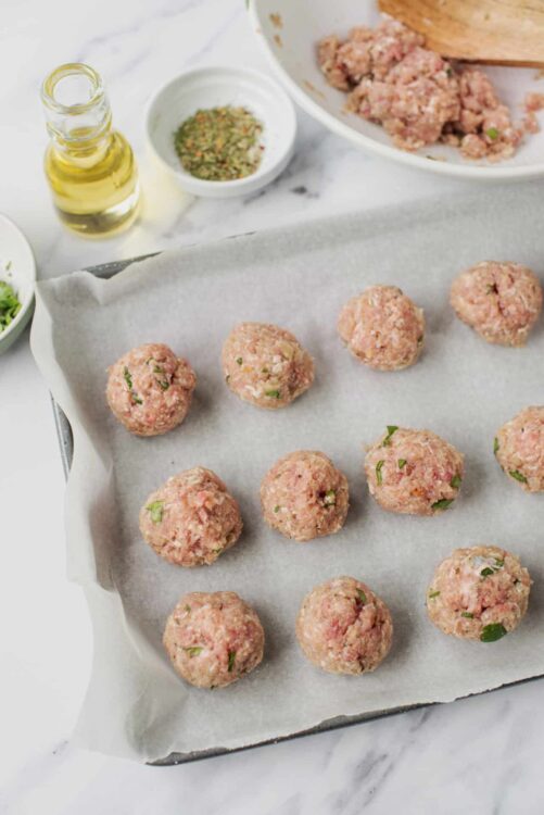 Raw meatballs with herbs on parchment paper before cooking.