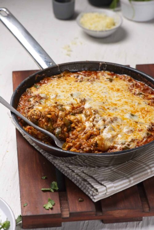 Comforting baked enchiladas with melted cheese in a cast iron skillet on wooden board.
