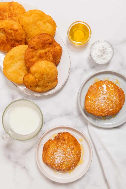 Golden fried chicken and crispy hash browns on a white marble surface with milk, oil, flour, and gravy.