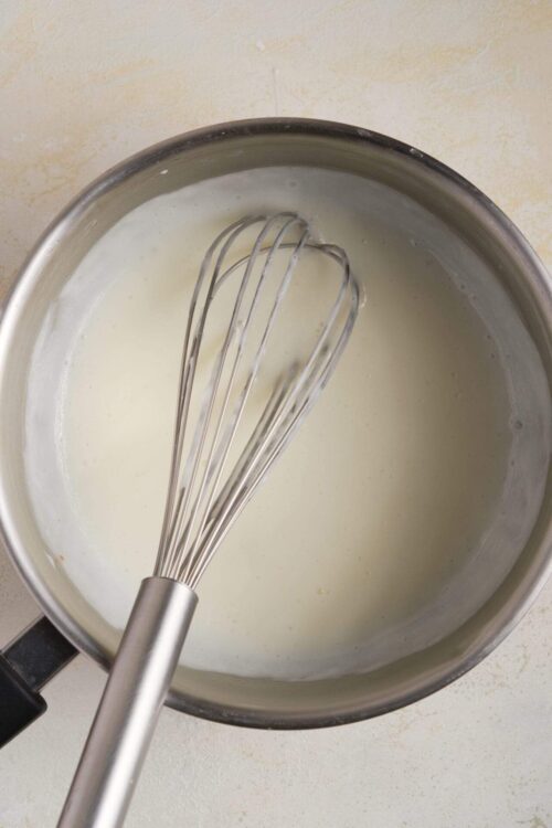 Cream being whisked in a stainless steel pot for baking recipes.