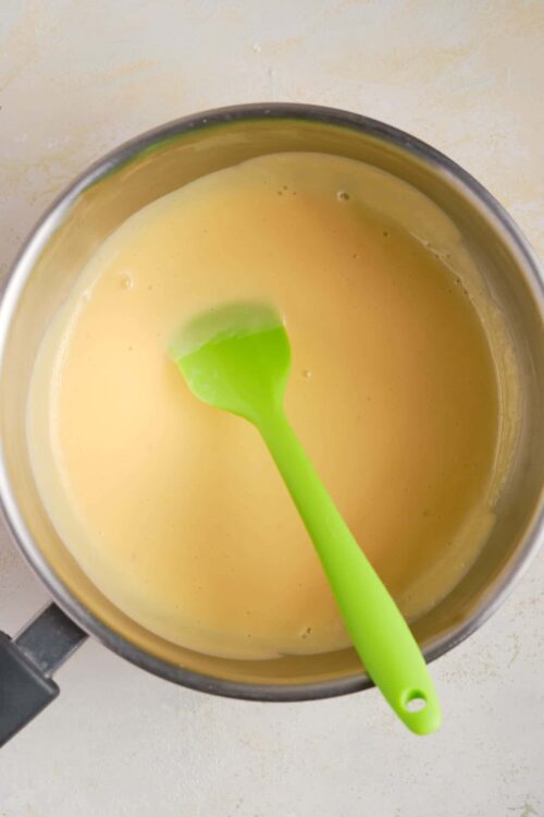 Smooth vanilla custard in a saucepan with a green spatula, ready for baking or dessert recipes.