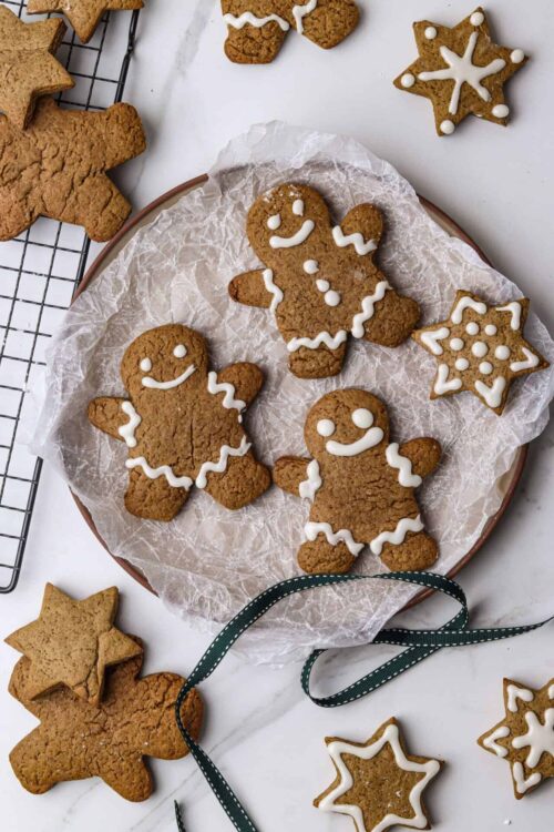 Gingerbread cookies decorated with white icing on a ceramic plate and baking sheet, perfect for holiday baking.
