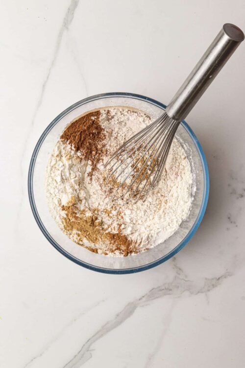 Flour and spices in a glass mixing bowl with a whisk, baking ingredients for cookie or cake batter.