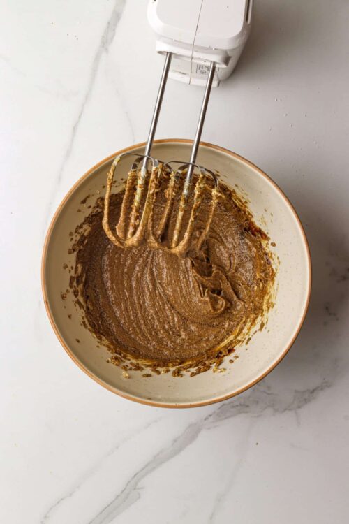 Rich chocolate cake batter in a mixing bowl with a hand mixer attached.