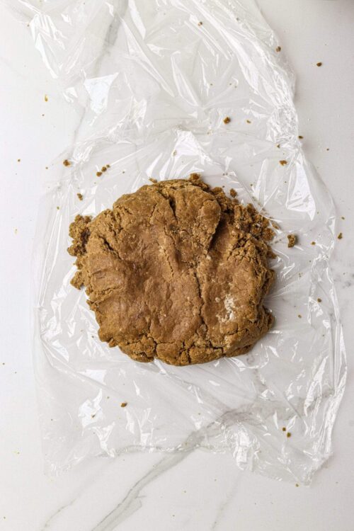 Cracked raw cookie dough on clear plastic wrap for baking or recipes.