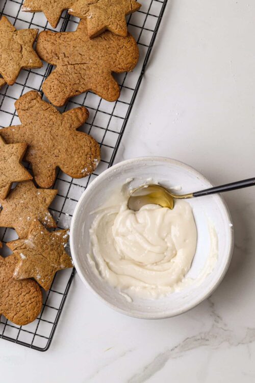 Gingerbread cookies and vanilla frosting on a wire rack and white marble surface.