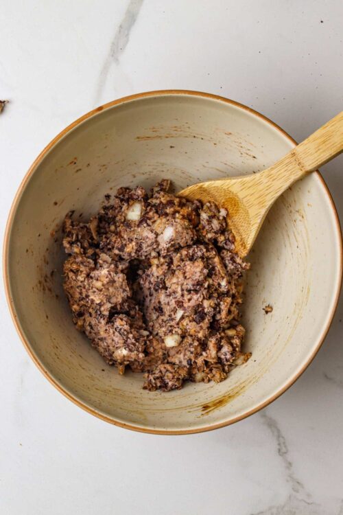 Crumbly chocolate banana muffin batter in a mixing bowl with wooden spoon.