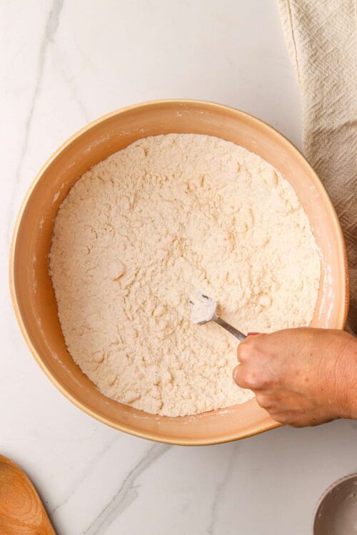 Flour mixture in a mixing bowl with a spoon, baking ingredients for homemade baked goods.