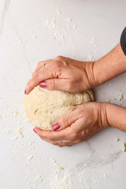 Buttery pie dough being kneaded by hands on flour-dusted surface for baking bread or pastries.