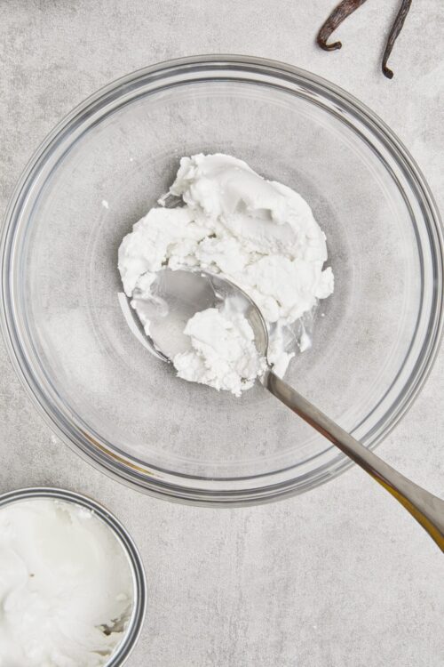 Fluffy cream cheese or mascarpone cheese in a glass mixing bowl for baking or dessert recipe preparation.