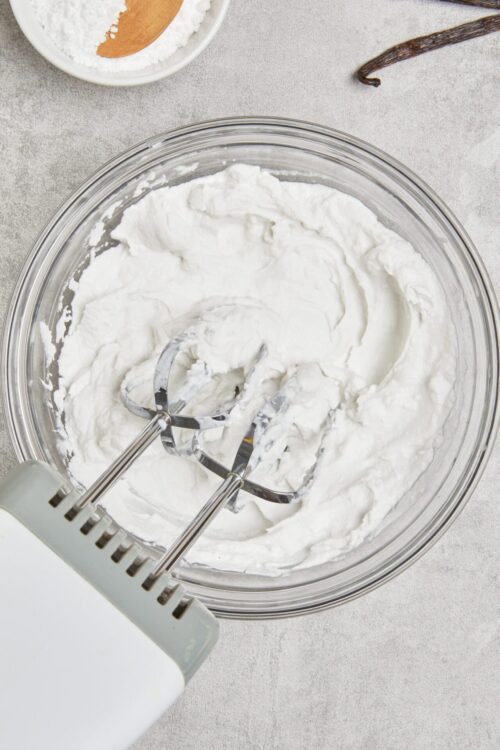 Fluffy homemade whipped cream in a glass mixing bowl with stand mixer beaters.